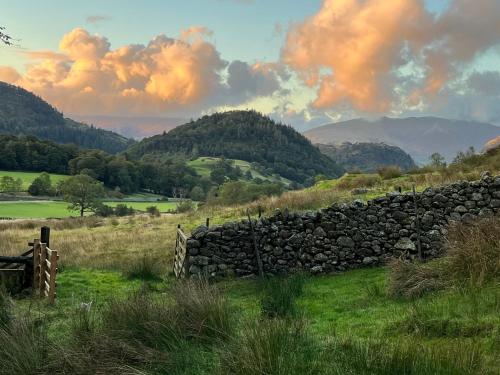 a stone fence in a field with mountains in the background at Stybeck Farm in Thirlmere
