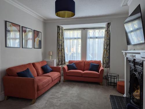 sala de estar con 2 sofás naranjas y chimenea en Spacious Family Holiday Home, en Porthcawl