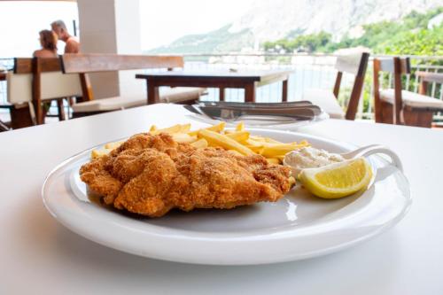 a plate with chicken and french fries and a lemon at Beach Hotel in Drasnice