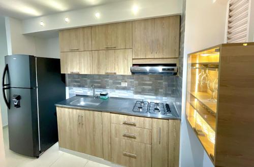 a kitchen with wooden cabinets and a black refrigerator at Apartamento con vista a las montañas, cerca Centro Comercial Mayales in Valledupar
