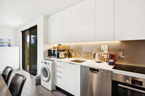 a kitchen with white cabinets and a washer and dryer at Rēhia at La residence du Parc in Queenstown