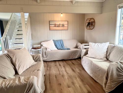 a living room with two couches and a staircase at Driftwood Retreat in Tutukaka