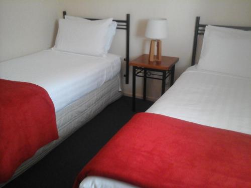 two beds in a hotel room with a red blanket at South Park Motel in Masterton