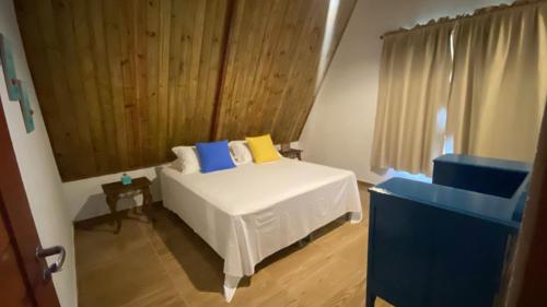 a bedroom with a white bed with blue and yellow pillows at Vila Feliz - Chalés completos - ideal para famílias in Serra de São Bento