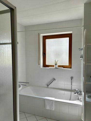 a white bathroom with a tub and a window at StrandGut in Uhldingen-Mühlhofen