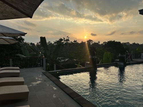 a swimming pool with the sun setting in the background at Brata Cottage Ubud in Ubud