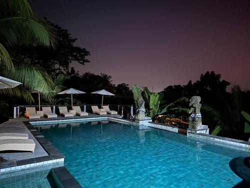 a large swimming pool with lounge chairs and umbrellas at Brata Cottage Ubud in Ubud