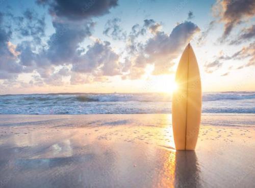 a surfboard standing on a beach with the sun setting at Chigasaki vacation house in Chigasaki