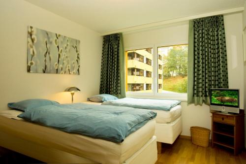2 łóżka w pokoju z telewizorem i oknem w obiekcie Residenz Ambassador B33 w mieście Leukerbad