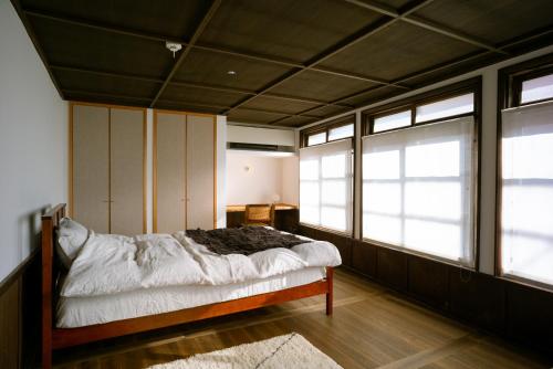 a bedroom with a bed with white sheets and windows at Une stay&diner in Sasayama