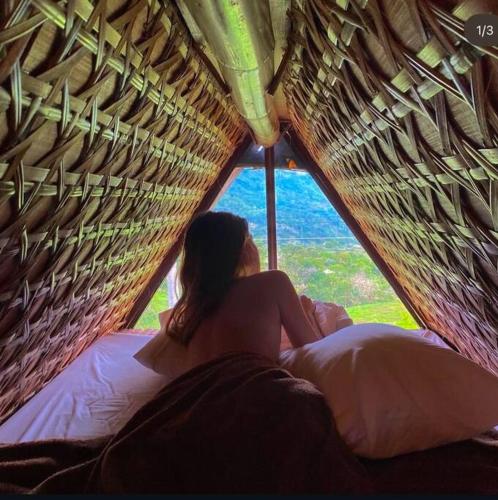 a woman sitting on a bed looking out a window at GAïA Cabinhouse in Cebu City