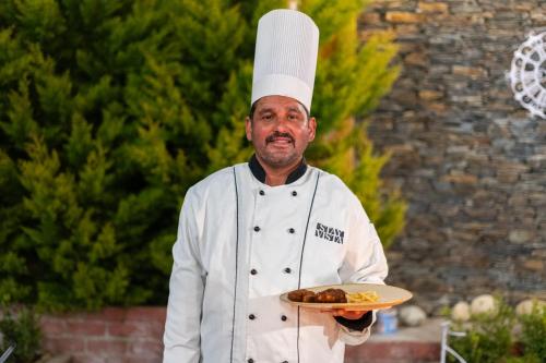 a man in a chefs hat holding a plate of food at StayVista at DAAFI House with Comp Breakfast in Theog