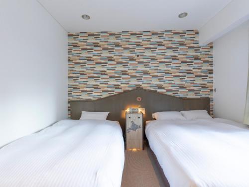two beds in a room with a brick wall at Tabist THE GREEN SAPPORO in Sapporo