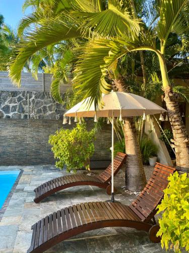 two benches with an umbrella next to a pool at Palm Nest in Rivière Noire