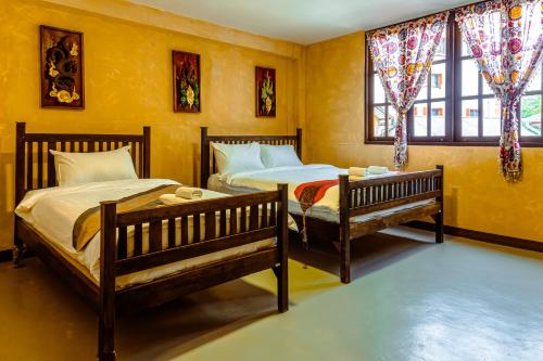 two beds in a room with yellow walls and windows at Eain in Chiang Mai