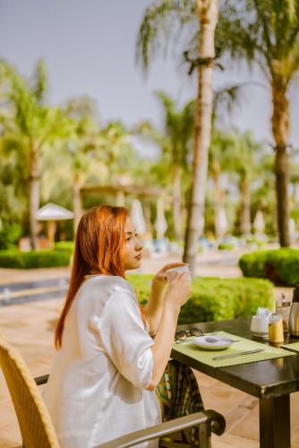 a woman sitting at a table with a cup of coffee at Pickalbatros Hôtel Du Golf - Adults Friendly 16 Years Plus- All-Inclusive in Marrakech
