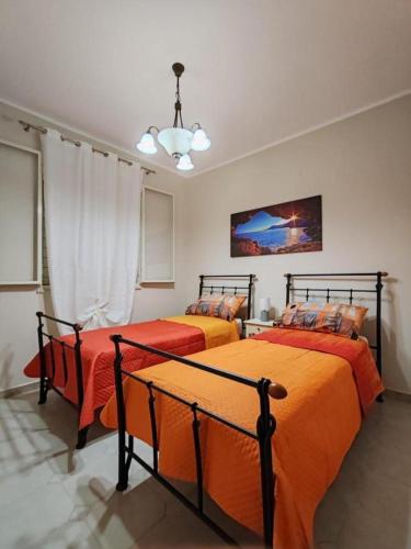 a bedroom with two beds with orange sheets and a chandelier at La Pergola Apartments in Lampedusa