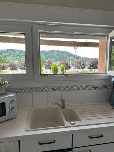une cuisine avec un évier et deux fenêtres dans l'établissement Le Gîte au bord du Lac, à Gérardmer