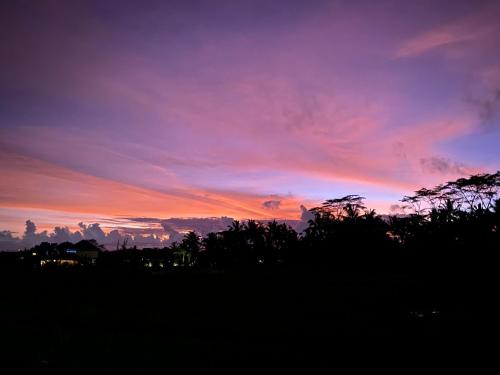 a sunset with trees in the foreground at Brata Cottage Ubud in Ubud