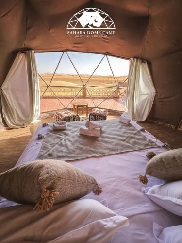 a bed in a tent with a view of the desert at Sahara Dome Camp in Merzouga