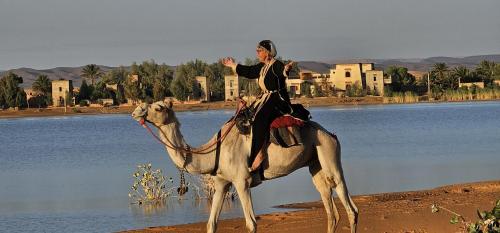 a woman riding on a camel next to a river at Sahara Dome Camp in Merzouga