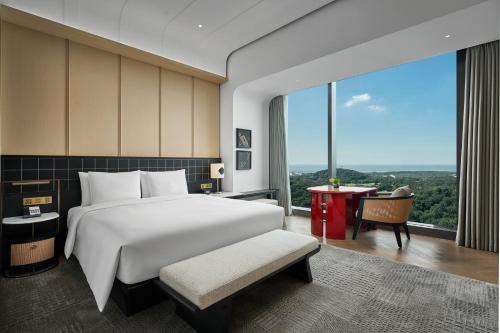 a bedroom with a bed and a desk and a large window at HUALUXE Shenzhen Bao'an in Shenzhen