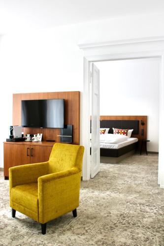 a living room with a yellow chair and a bed at Hotel Alma Am Anger in Erfurt