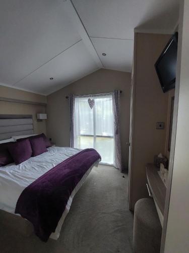 a bedroom with a bed with purple pillows and a window at Tulip Lodge at Oakdene - Passes included free! in Ferndown