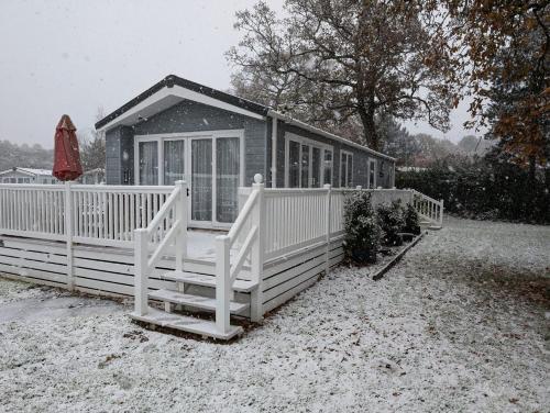 a small house with a white fence in the snow at Tulip Lodge at Oakdene - Passes included free! in Ferndown