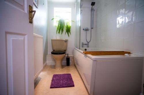 a bathroom with a toilet and a tub and a purple rug at Coastal Terrace Retreat- Allocated Parking, 2 Bedrooms in Portsmouth