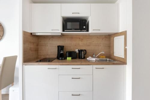 une cuisine avec des armoires blanches et un micro-ondes dans l'établissement OVELIA Epinay-sur-Orge - Le Grand Marronnier, à Épinay-sur-Orge