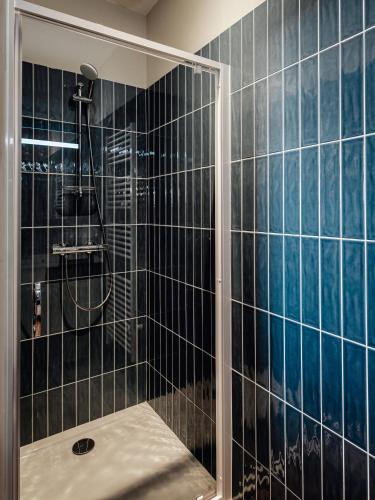 La salle de bains est pourvue d'une douche et de murs carrelés noirs. dans l'établissement Maison Bleue Est 12 personnes, à Saint-Julien-en-Born