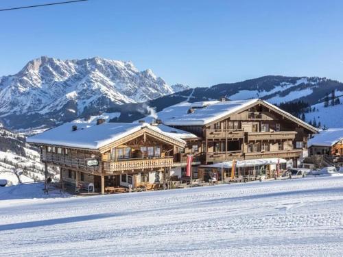 a large wooden building in the snow with mountains at Berggasthof Christernreith in Maria Alm am Steinernen Meer