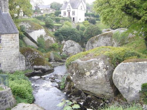 a river with rocks and a house in the background at Les gîtes de la vallée du rivoal in Lopérec
