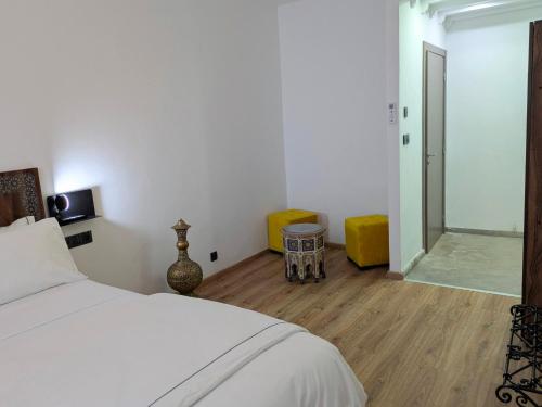 a bedroom with a white bed and a room with yellow chairs at Hôtel Les Remparts in Azemmour