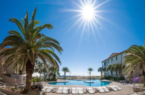 a resort with a pool and palm trees and chairs at Beach Club Gulf Front 3B Condo - 2003 in Pensacola Beach
