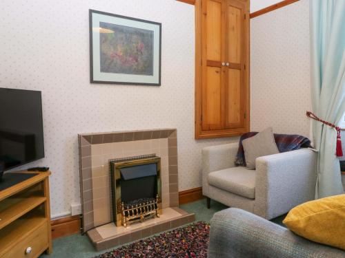a living room with a fireplace with a chair and a television at 3 Mountain View in Sedbergh