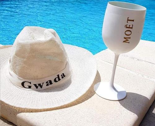 a hat and a straw wine glass next to a pool at Villa du bonheur in Goyave