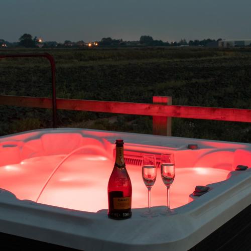 a bottle of wine and two wine glasses in a hot tub at Holly Lodge - Quirky Shepherd's Hut With Hot Tub - Bespoke Made From A Salvaged Railway Carriage in Boston