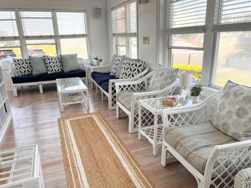 a living room with white chairs and tables and windows at Windward at the Beach in Beach Haven