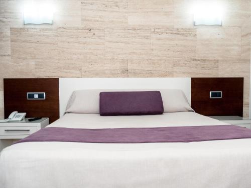 1 dormitorio con 1 cama blanca grande con almohada morada en Escuderos Hotel Cruz, en Argamasilla de Calatrava