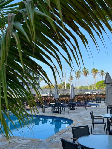 a resort pool with tables and chairs and palm trees at Aláfia Porto de galinhas Mana beach in Porto De Galinhas