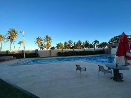 a pool with two chairs and a table and an umbrella at Casa aconchegante perto da praia in Salvador
