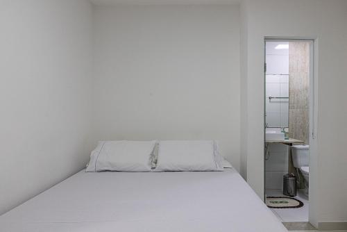 un letto bianco in una stanza bianca con specchio di 2 suítes a 500m da Praia dos Milionários a Ilhéus