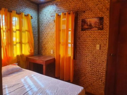 a bedroom with a bed and yellow curtains and a table at MarineroTravellers Inn in San Vicente
