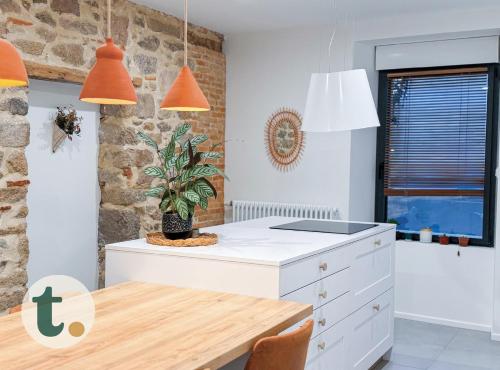 une cuisine avec une table et des lampes suspendues orange dans l'établissement Tranquiloue - Maison au charme d'Antan - PuyduFou, à Les Landes-Génusson