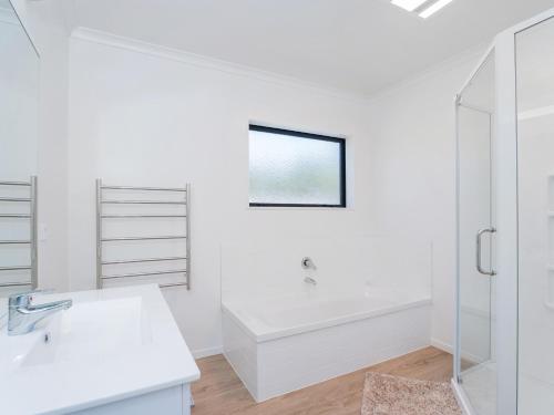 a white bathroom with a tub and a sink at Family Casa - Cooks Beach Holiday Home in Cooks Beach