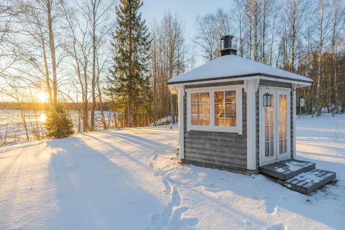 a small building in the snow with the sun in the background at The Haven of Riverside - Villa Sieripirtti in Rovaniemi