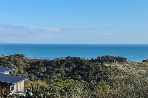 a house on a hill with the ocean in the background at The 'Flax Pod' cabin in Pohara, amazing sea views in Pohara