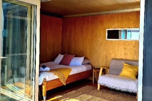 a small bedroom with a bed and a chair at The 'Flax Pod' cabin in Pohara, amazing sea views in Pohara